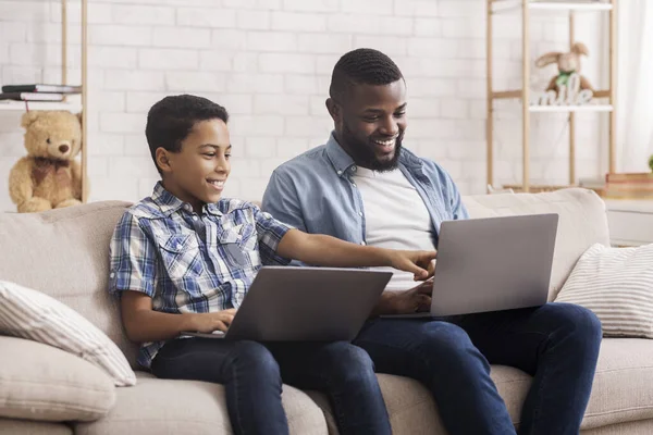 Juegos en línea. Afro hijo y papá jugando en computadoras portátiles en casa — Foto de Stock