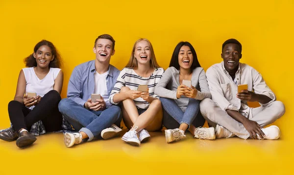 Laughing group of multiracial classmates holding smartphones — ストック写真