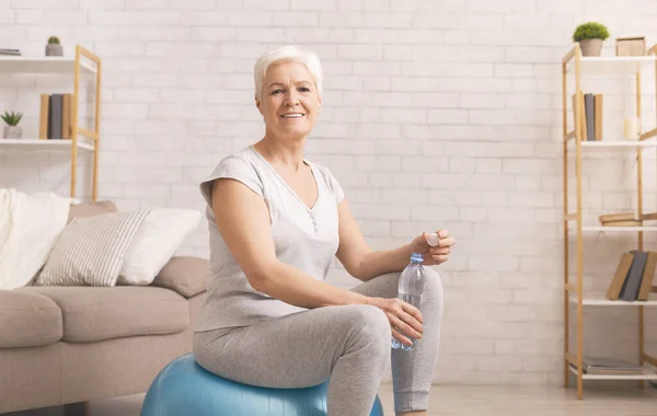 Alegre mujer mayor bebiendo agua en fitball, espacio libre — Foto de Stock