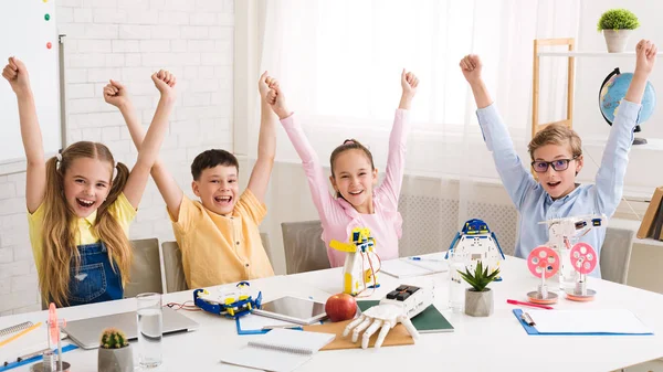 Niños alegres animando y levantando las manos en la clase de robótica — Foto de Stock