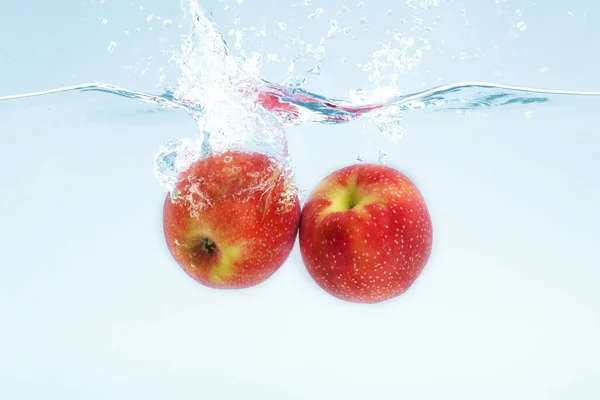 Due mele rosse mature che cadono in acqua con spruzzi su sfondo blu — Foto Stock
