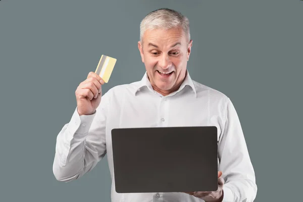 Happy mature man holding card and personal computer — Stock fotografie