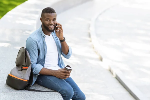 Handsome black man talking on cellphone outdoors and drinking takeaway coffee — Zdjęcie stockowe