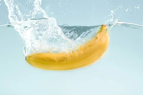Plátano dulce en agua salpicada sobre fondo azul —  Fotos de Stock