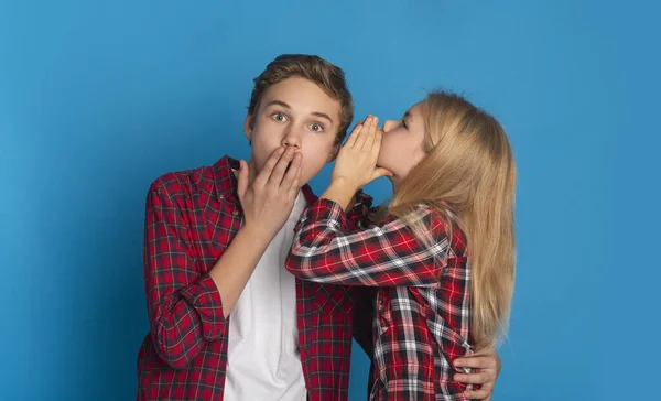 Little Sister Sharing Secret With Her Teen Brother On Blue Background — Stockfoto