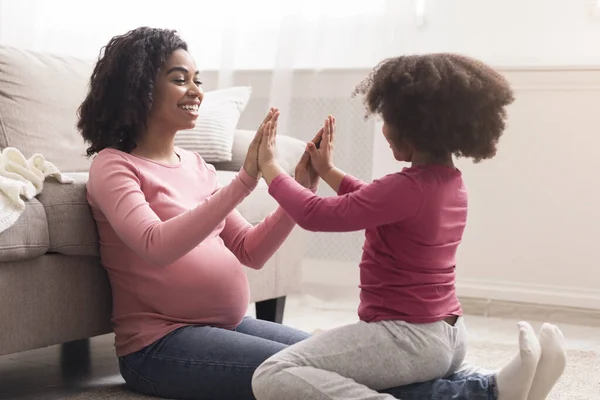Happy little girl playing with pregnant black mom in living room — Stock Fotó