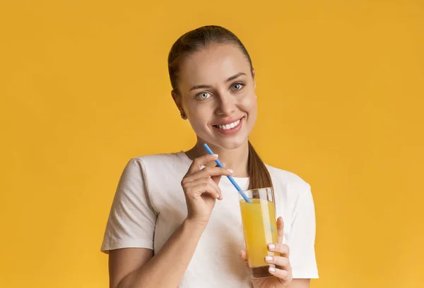 Pretty young woman with glass of orange juice over yellow background — Stok fotoğraf