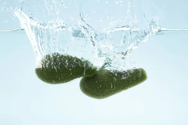 Fresh tropical fruits. Two delicious avocados falling into clear water with splashes on blue background — Stockfoto