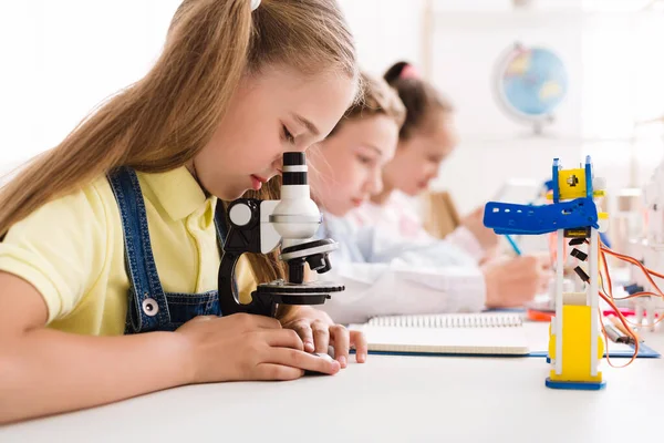 Schoolgirl looking at microscope at stem robotic class — Stock Photo, Image