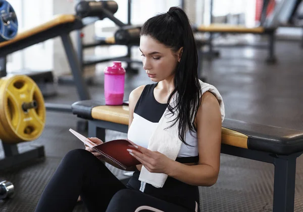 Workout planning. Young woman with notebook resting after training in gym — Stockfoto