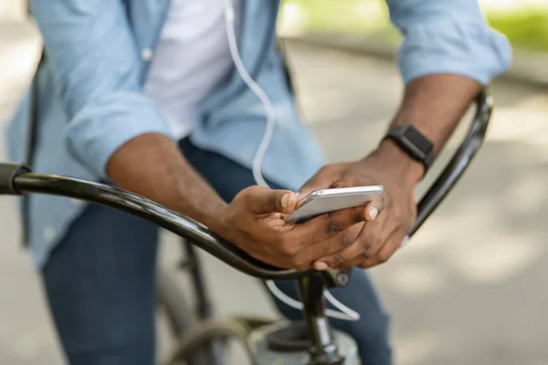 Unrecognizable man on bicycle holding smartphone and listening music in earphones — Zdjęcie stockowe