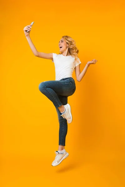 Overjoyed woman jumping and taking selfie on phone — 图库照片