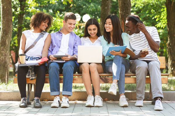 College Students With Laptop Preparing For Lessons On Bench In Campus