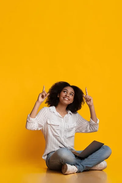 Excited black woman sitting with laptop on floor and pointing upwards — Stock Photo, Image