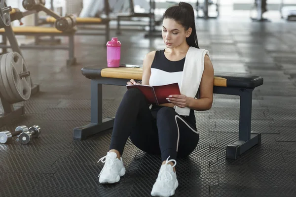 Mujer atractiva con cuaderno planeando su horario de entrenamiento en el club deportivo — Foto de Stock