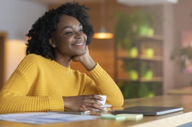 Excited afro girl dreaming about prosperous future, drinking tea
