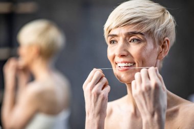 Lady Flossing White Teeth Standing Wrapped In Towel In Bathroom