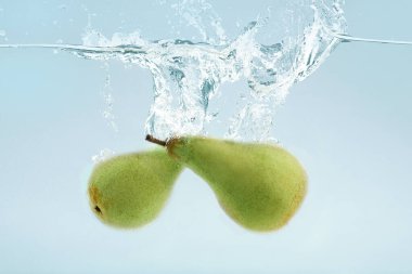 Two green pears falling into transparent water on blue background