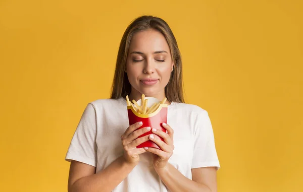 Portrait of satisfied young woman with french fries serving in hands — ストック写真