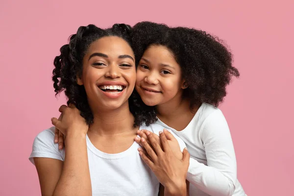 Feliz africano mamá posando con su adorable hija en rosa fondo — Foto de Stock