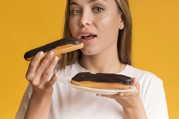 Mujer joven comiendo Eclairs con crema de chocolate y mirando a la cámara — Foto de Stock