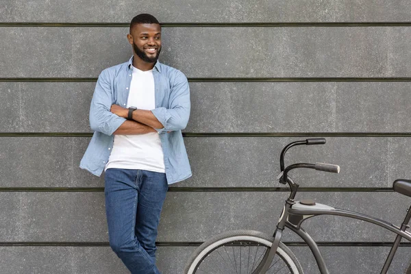 Jovem negro posando ao lado de bicicleta sobre parede de concreto urbano — Fotografia de Stock