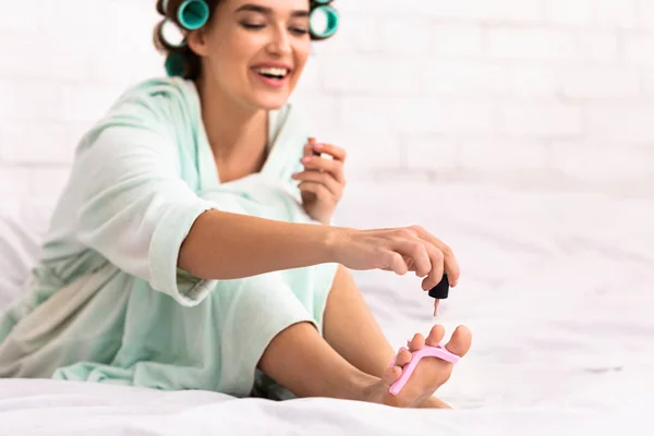 Cheerful Girl With Curlers Making Pedicure Sitting In Bed Indoor — Stockfoto