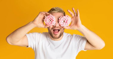 Adam eğleniyor, gözünün önünde donut tutuyor.