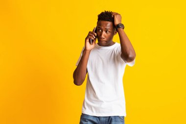 Şok olmuş genç Afrikalı adam cep telefonuyla konuşuyor.