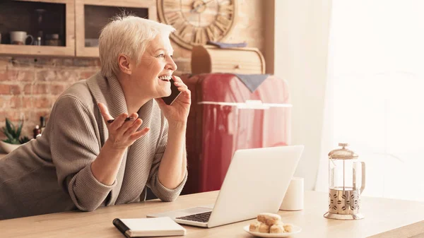 Surpised starý žena mluví na mobilní telefon v kuchyni a emocionálně gesta — Stock fotografie