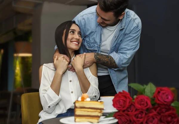 Namorado abraçando namorada fazendo surpirse e dando buquê no café — Fotografia de Stock