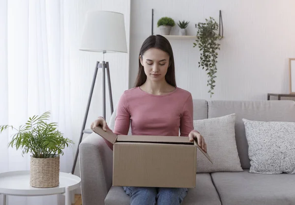 Vrolijk meisje uitpakken kartonnen postpakket in de woonkamer — Stockfoto