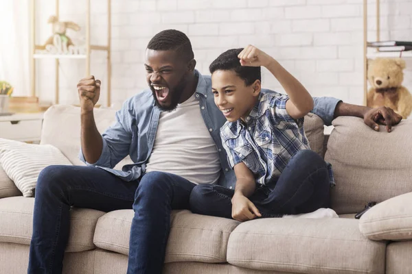 Afro pai e filho assistindo esportes na TV e emocionalmente torcendo — Fotografia de Stock