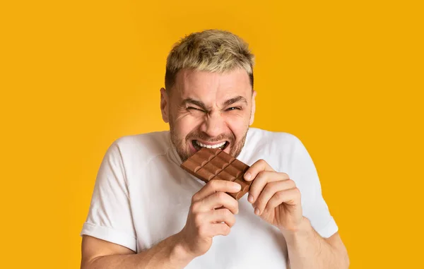 Homem doce dente felizmente morde chocolate isolado no fundo amarelo — Fotografia de Stock