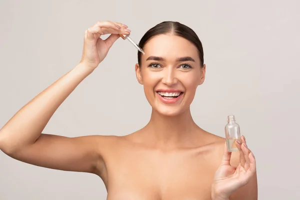 Le flicka tillämpa kosmetisk olja på ansiktet stående i studion — Stockfoto