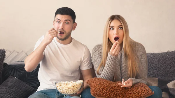 Überraschtes junges Paar mit Popcorn vor dem Fernseher im Wohnzimmer — Stockfoto