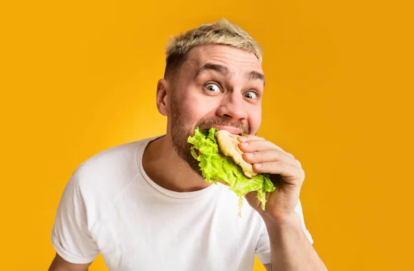 Lustiger Typ, der einen Burger isst, Augen weit auf — Stockfoto