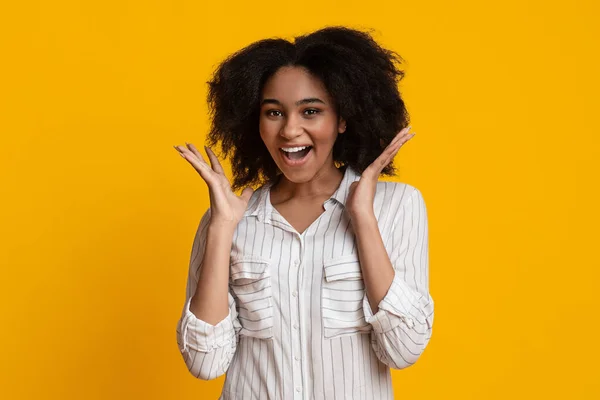 Freudige Afro-Frau hebt erstaunt die Hände und lächelt in die Kamera — Stockfoto