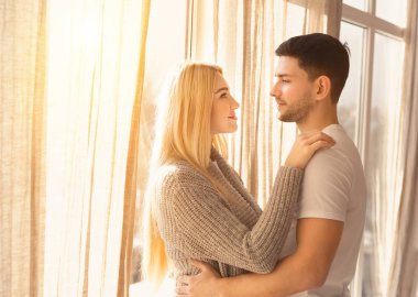 Işık odasında pencerenin yanında kucaklaşan genç çift, boşluğu kopyala