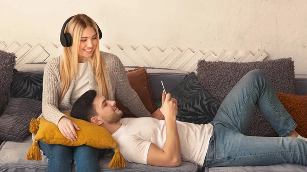 Casal amoroso com fones de ouvido e telefone celular no sofá em casa — Fotografia de Stock