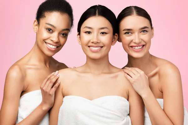 Drie prachtige meisjes poseren in bad handdoeken op roze achtergrond — Stockfoto