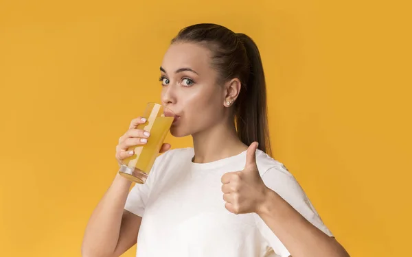 Susamış genç bir kadın taze portakal suyu içiyor ve baş parmağını kaldırıyor. — Stok fotoğraf