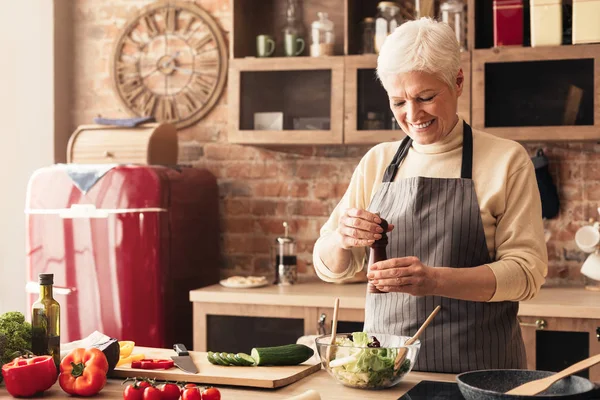 Fröhliche Seniorin würzt frischen Salat mit Pfeffermühle — Stockfoto