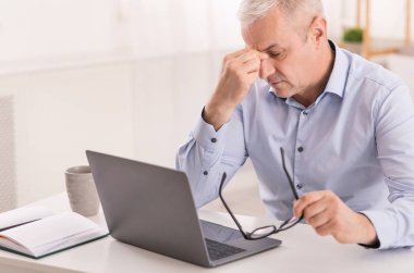 Üst düzey yönetici dizüstü bilgisayar kullanırken burnuna masaj yapıyor
