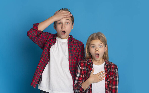 Shocked brother and sister standing with opened mouth over blue background