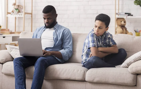 Pequeño negro hijo ofendido a su padre ocupado con el ordenador portátil — Foto de Stock
