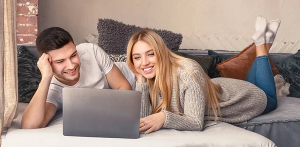 Adorável jovem casal com laptop deitado no sofá na sala de estar — Fotografia de Stock