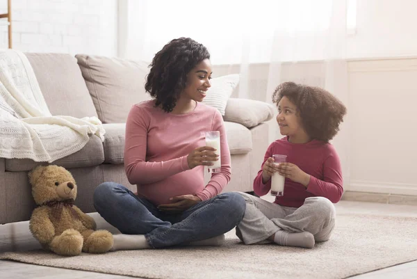 Щаслива чорна мама і маленька дочка п'ють молоко у вітальні — стокове фото