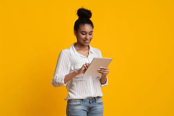 Glimlachend Afrikaans meisje met behulp van digitale tablet, staande over gele achtergrond — Stockfoto