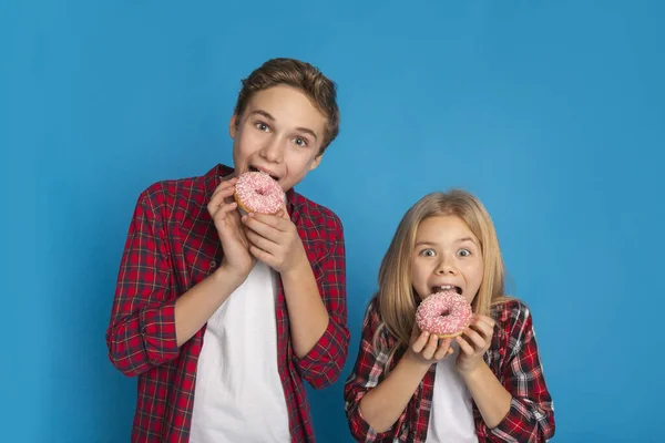 Нездоровый Свитс. Preteen Brother and Sister Eating Donuts On Blue Background — стоковое фото